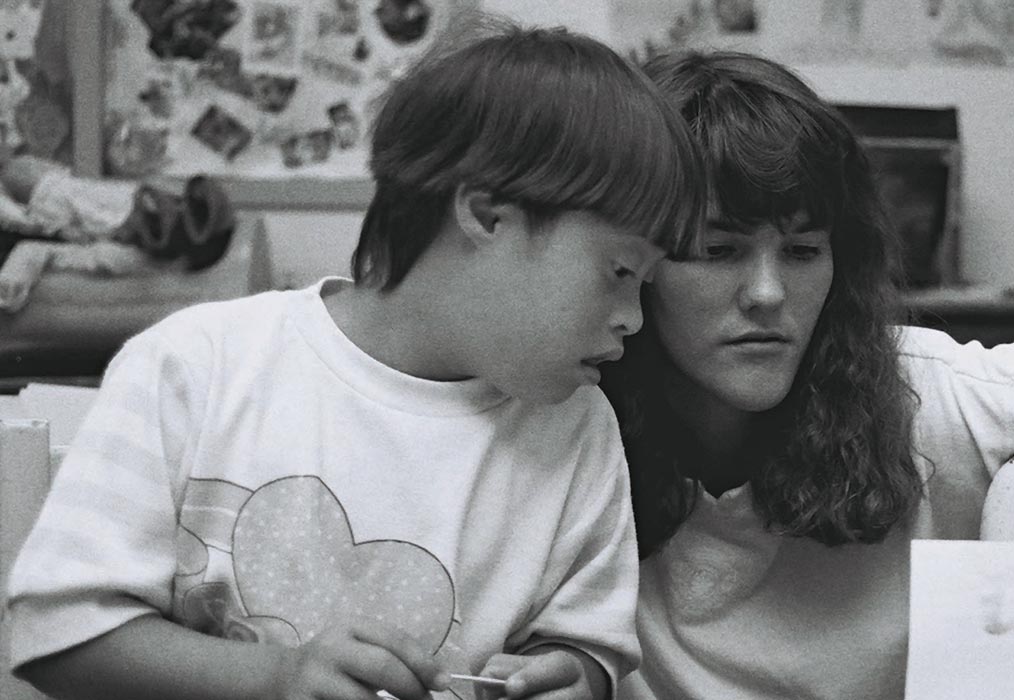 Woman working with a child with disability, looking at a paper together in a learning setting.
