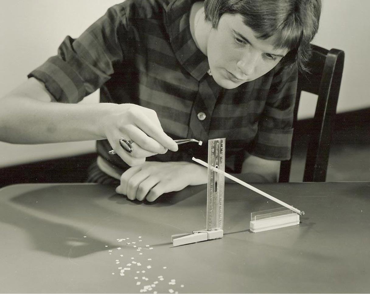 Black and white photo of a young woman working on a physics project.