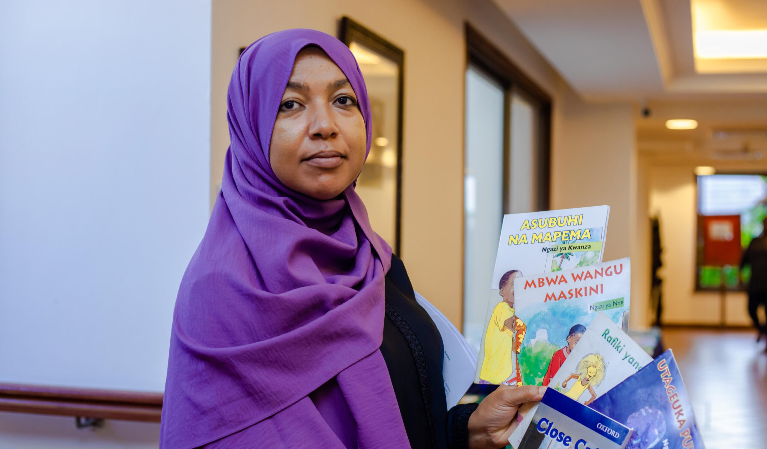 Woman wearing a purple hijab looking at the camera, holding books in her hand.