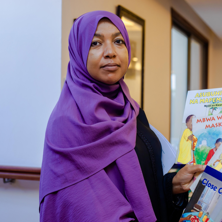 Woman wearing a purple hijab looking at the camera, holding books in her hand.
