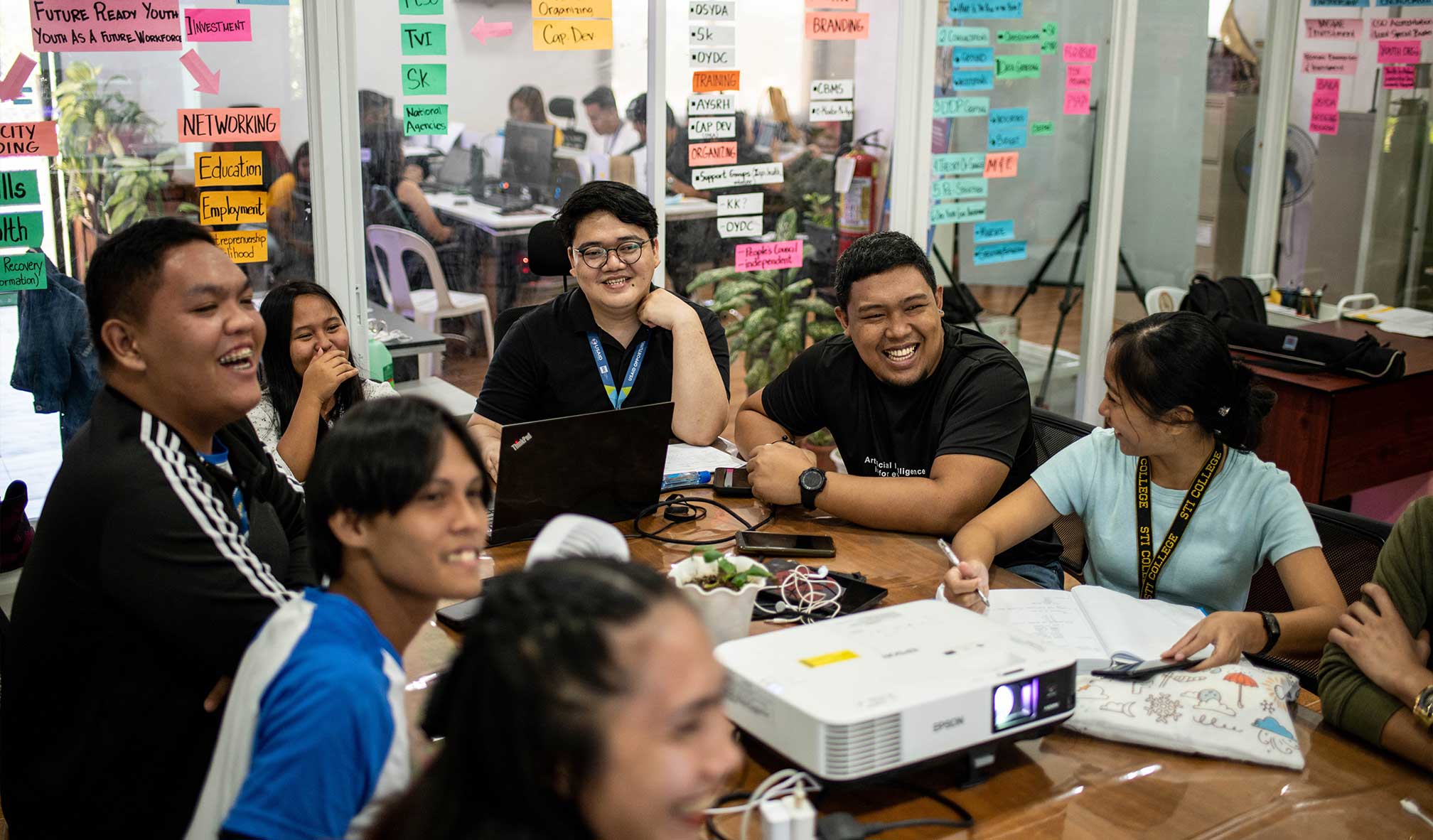 Group of youth sitting around a table, smiling in a learning setting.
