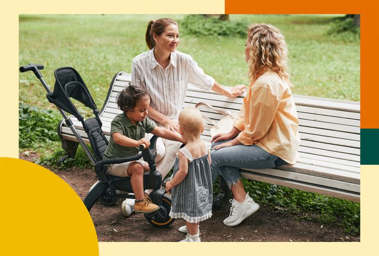 Two women seated on a bench facing each other, talking, while two young kids interact in front of them—one in a stroller and one standing.
