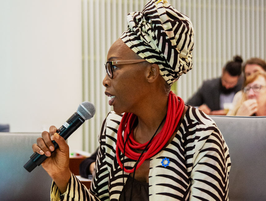 Woman speaking into a microphone, dressed formally in a conference setting.