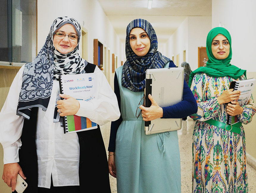 Three women smiling at the camera, holding education manuals and binders.