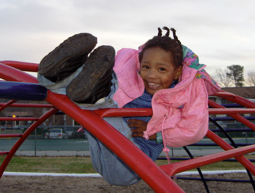 Small child sitting safely on top of a playground structure.