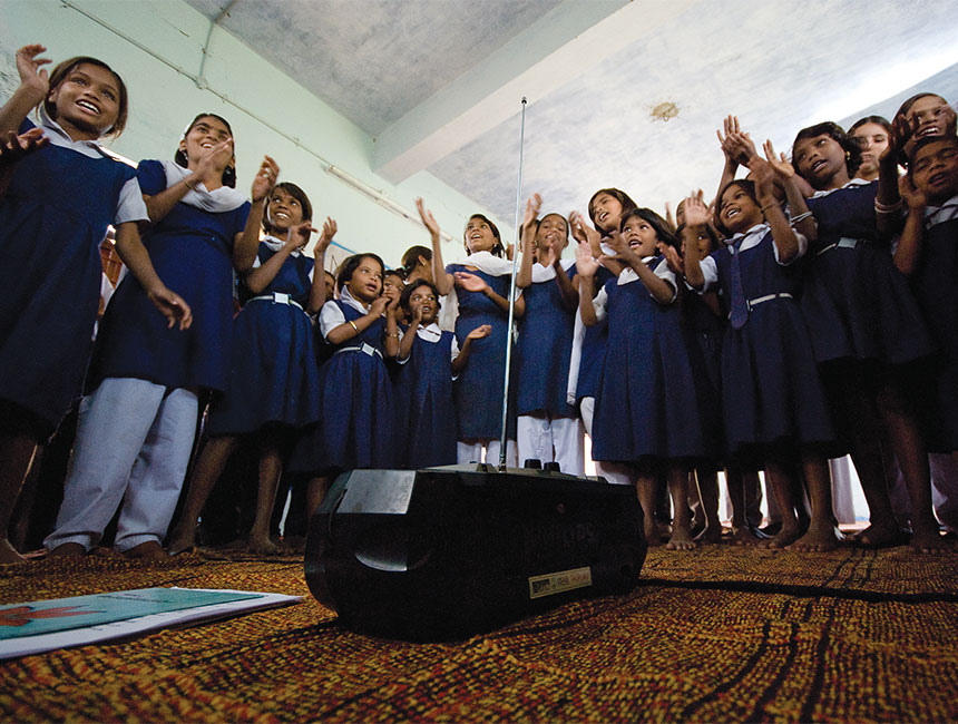 Group of children in uniforms engaged in a learning setting with interactive audio instruction at the center.