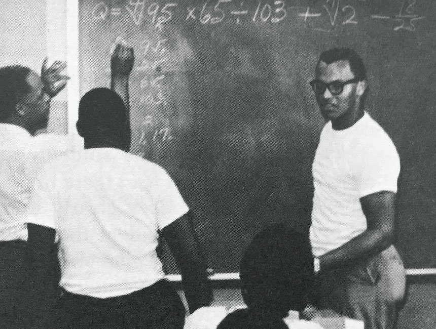 Black and white photo of four men working together at a chalkboard on a math problem.