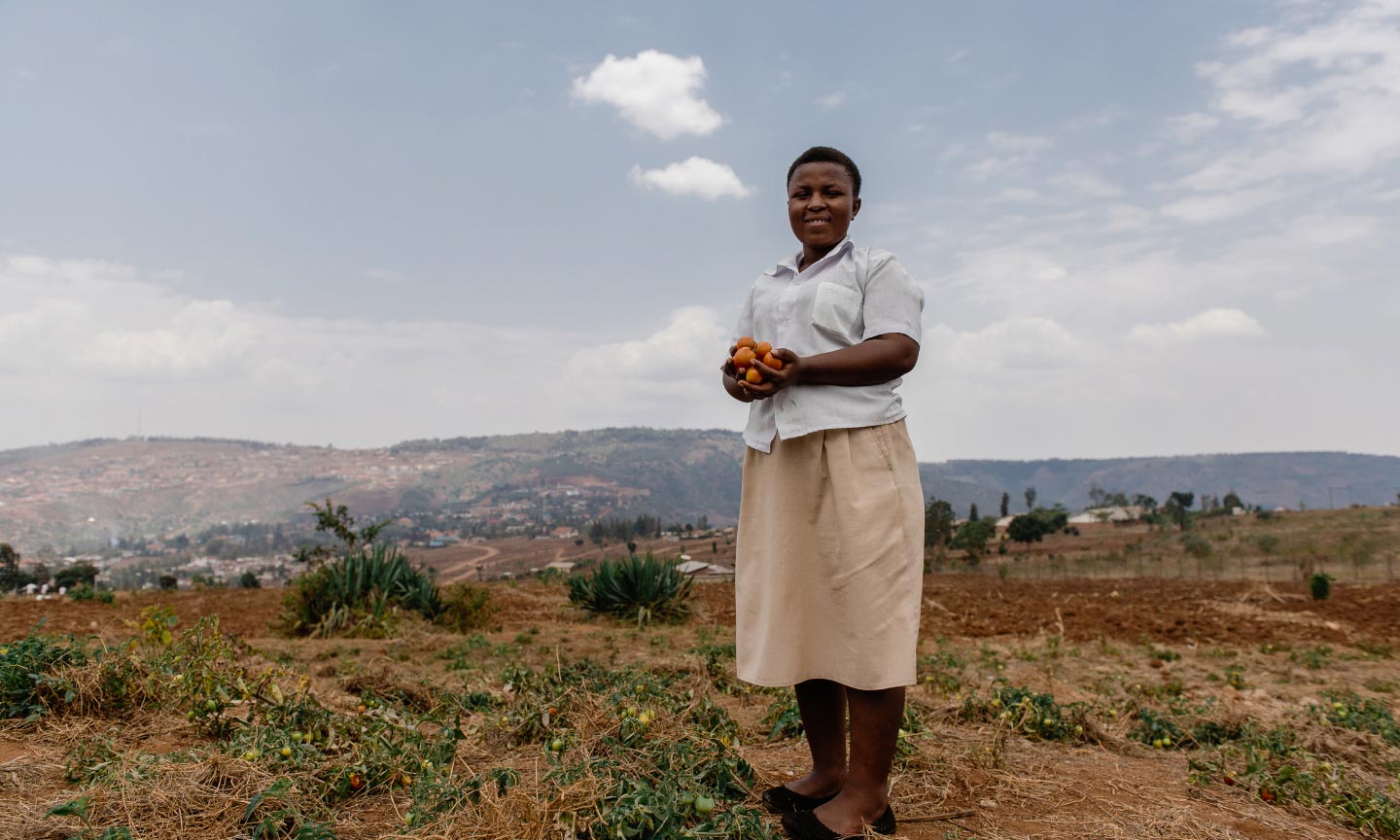 Woman standing in an open field with a vast landscape behind her.