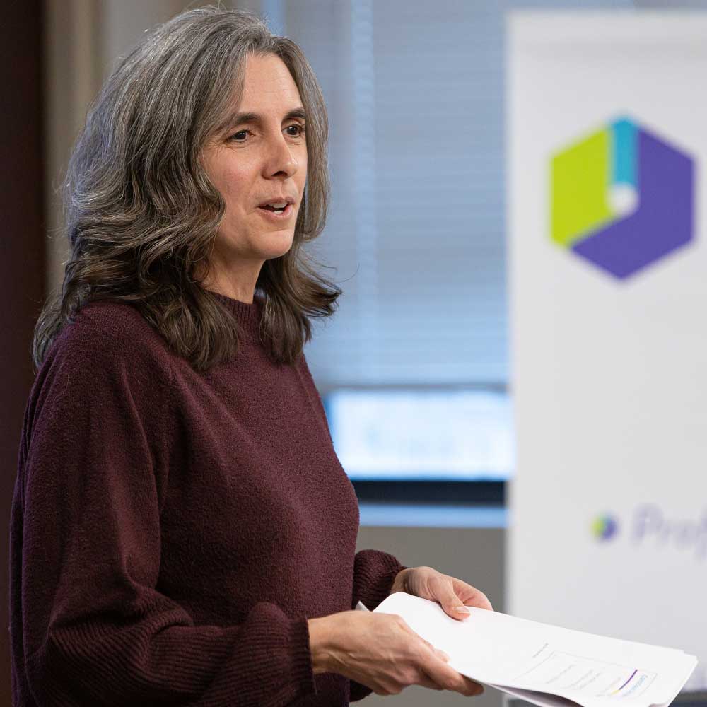 EDC employee speaking to a room and holding a stack of paper