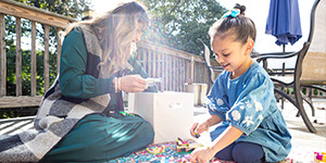 Researcher evaluating a young child playing outside on a mat.