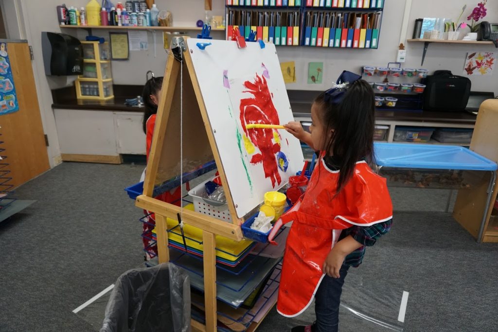 Young child painting at an easel in a classroom.