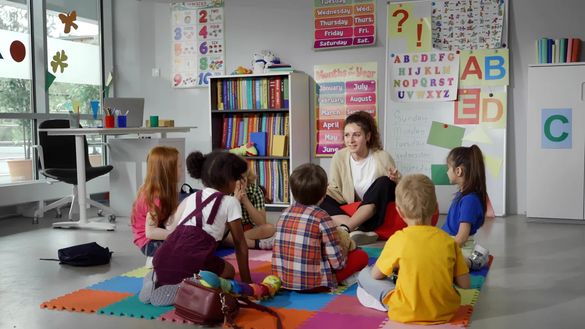 Adult seated on the floor with six young children in a learning setting.