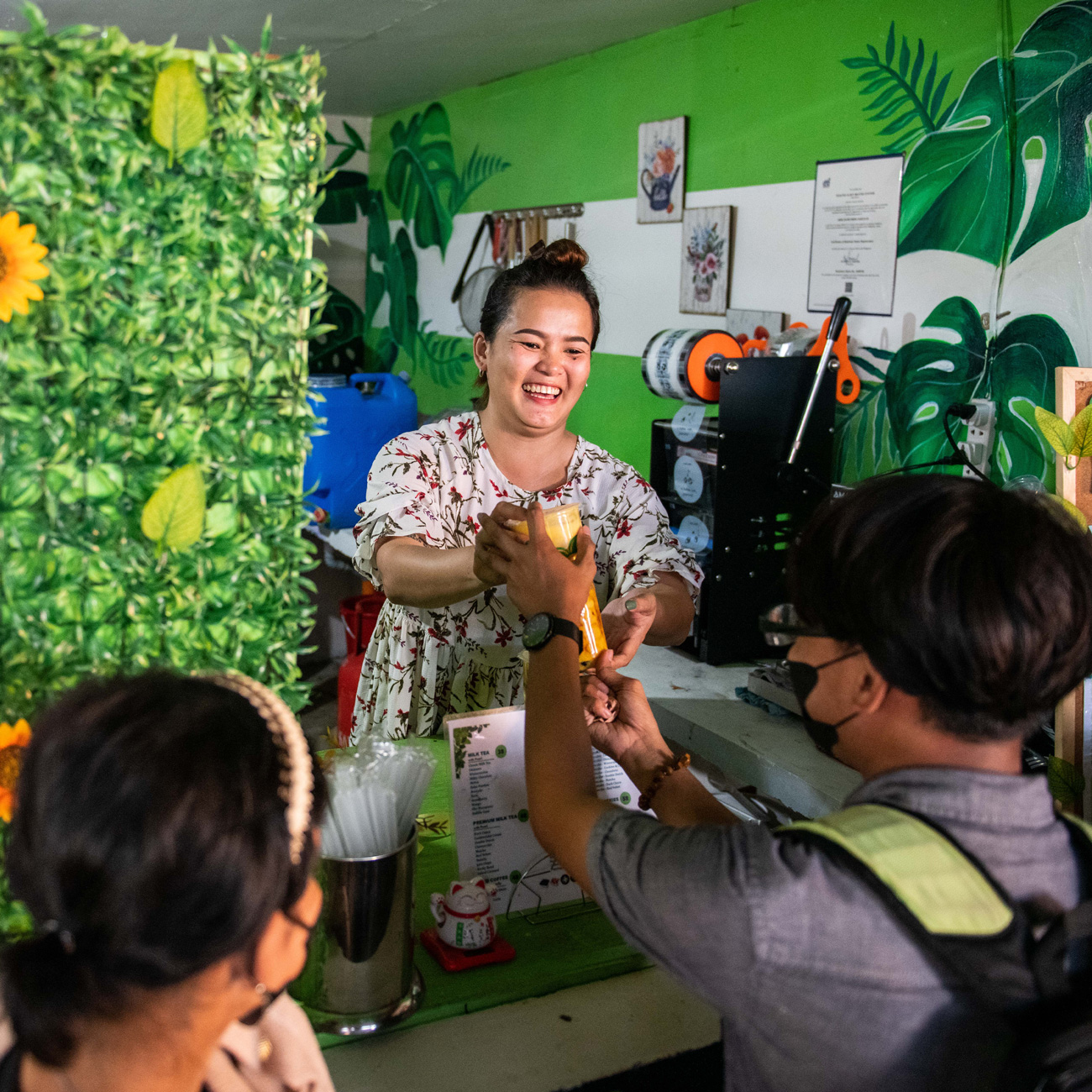 Woman handing juice to customers across a counter, in a setting that emphasizes service skills and customer interaction.