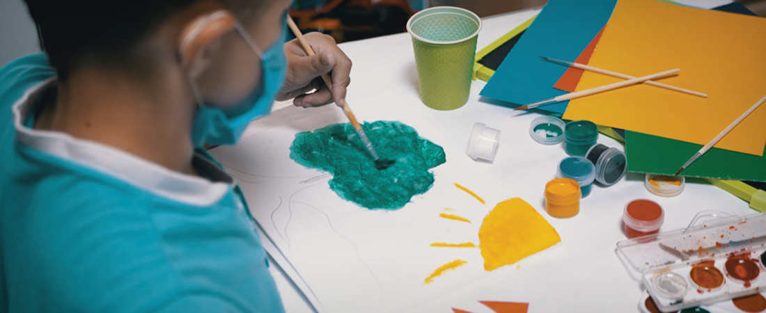 A photo of a student painting a tree crown while wearing a face covering.