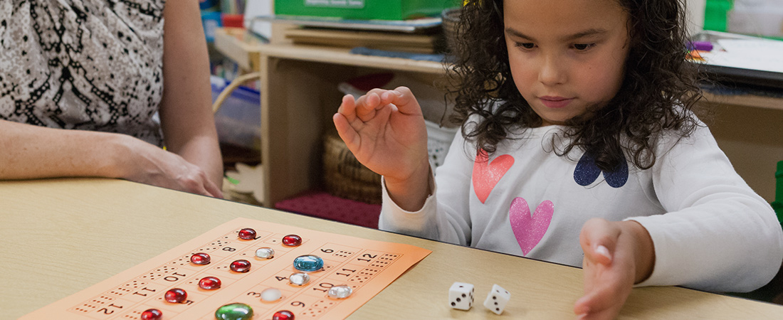 A photo of a preschooler playing a math game with two dices and colorful beads