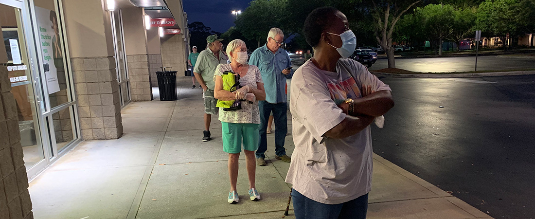 A photo of elderly individuals with face coverings standing on a sidewalk.